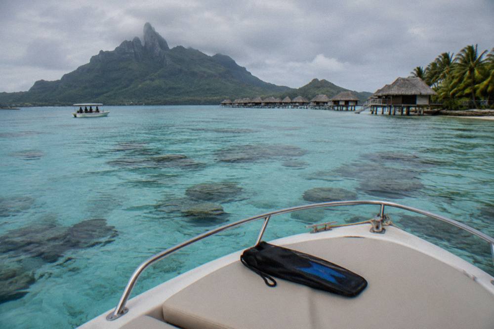 Small boat anchored over a shallow coral garden in bright turquoise lagoon water