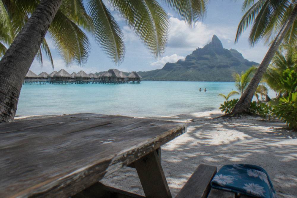 Wooden picnic table under palm shade on a small motu island beside calm lagoon water