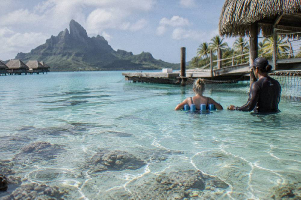 Guide assisting a guest holding a flotation belt in shallow lagoon water