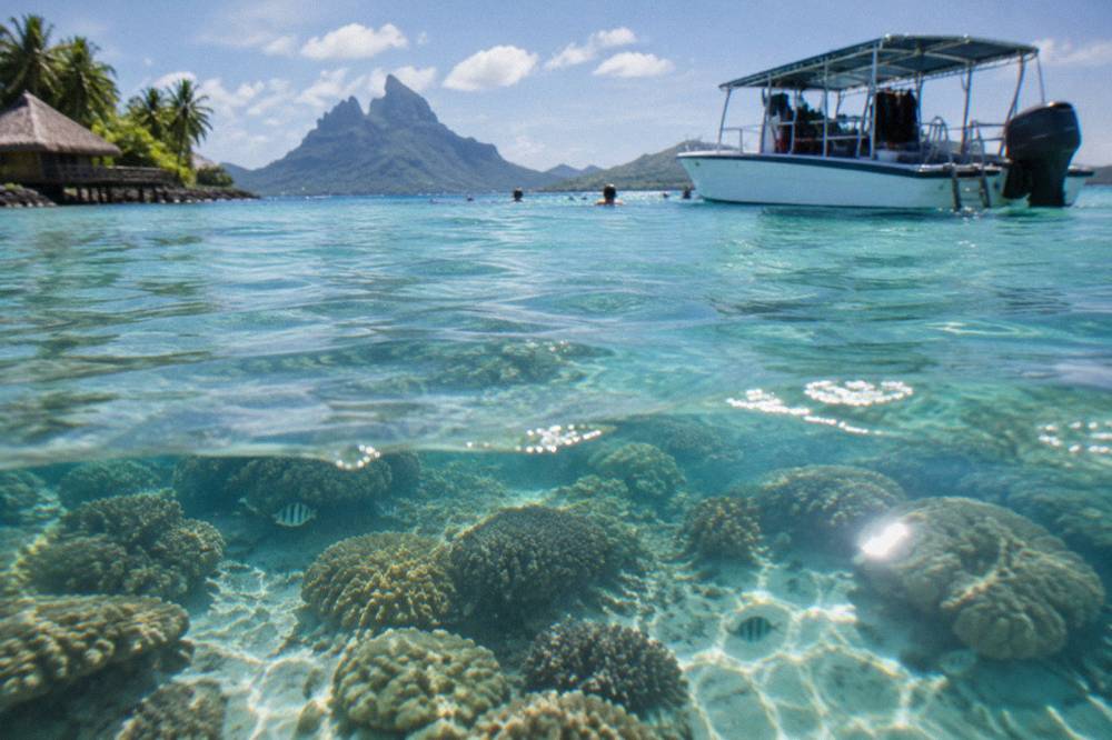Snorkel boat anchored near shallow coral water with passengers in the water beside the hull