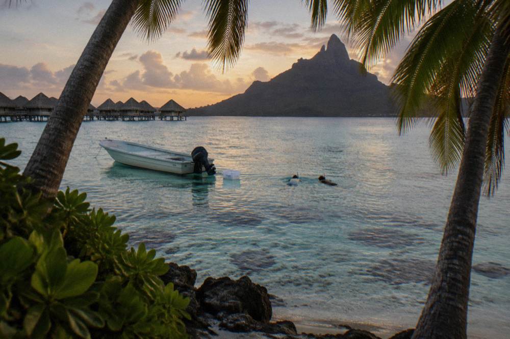 Small boat with snorkelers floating above pale coral in clear shallow lagoon water