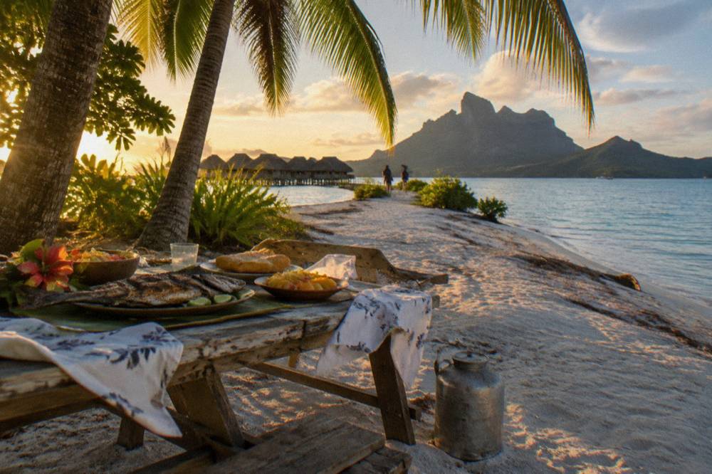 Wooden picnic table set with lunch on a sandy tropical islet