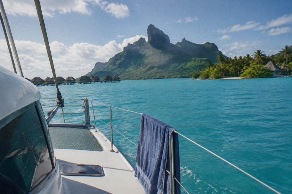 A catamaran sailing across a calm lagoon with green volcanic peaks in the background