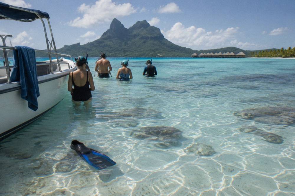 Guests in snorkel gear beside a small boat in clear shallow lagoon water