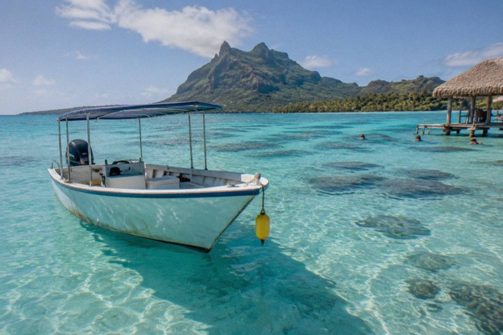 A small boat anchored over a shallow coral reef in clear turquoise lagoon water