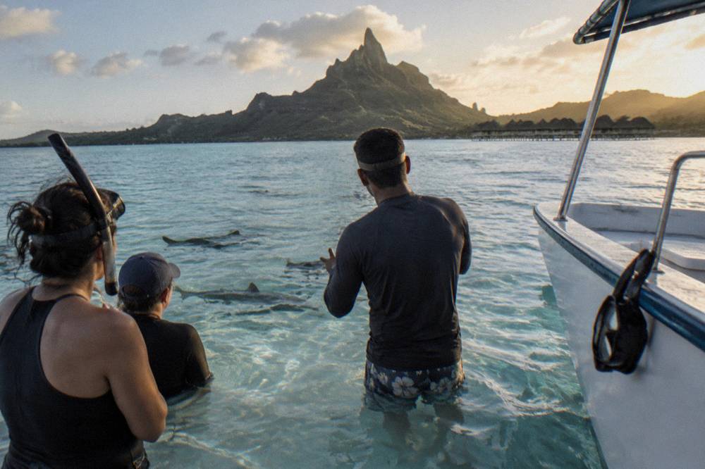 A guide briefing snorkelers beside a small boat anchored over a shallow lagoon sandbar
