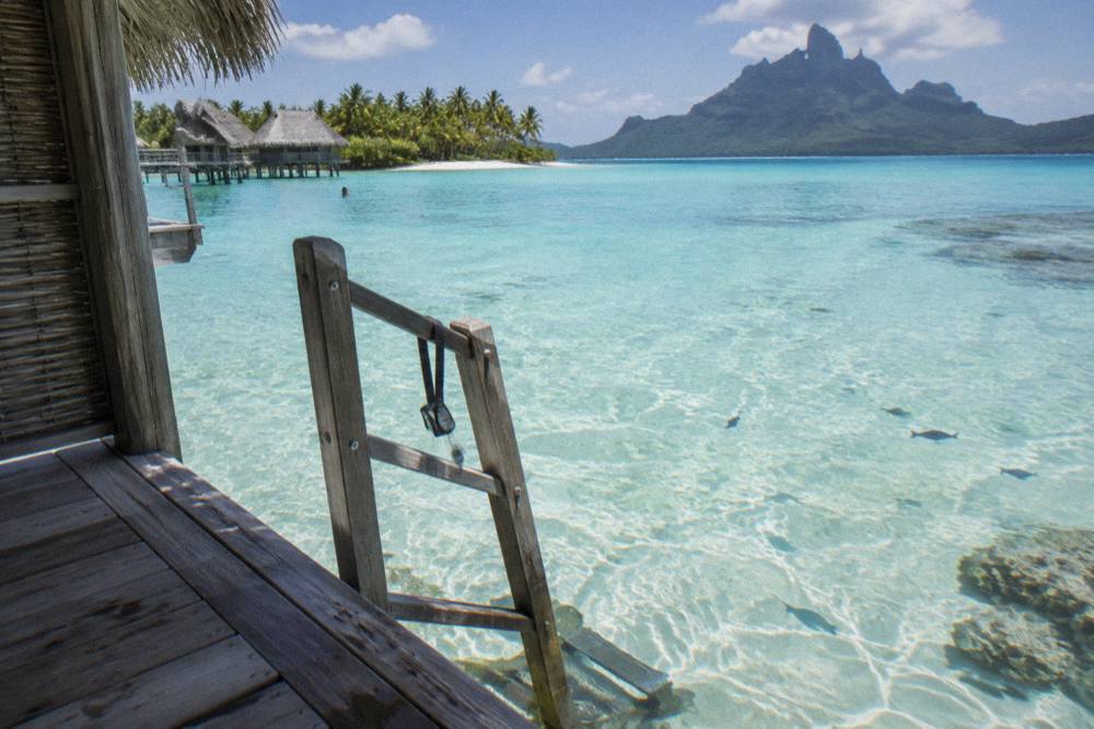 View from an overwater bungalow deck of clear shallow lagoon water over pale sand