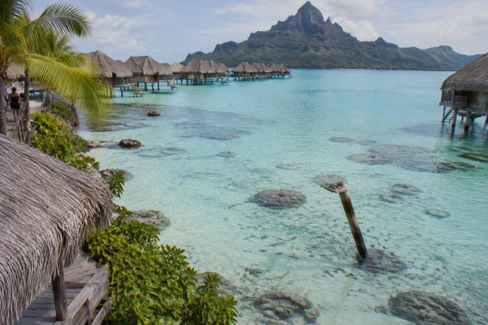 Shallow turquoise lagoon water over pale sand with scattered coral heads visible from above