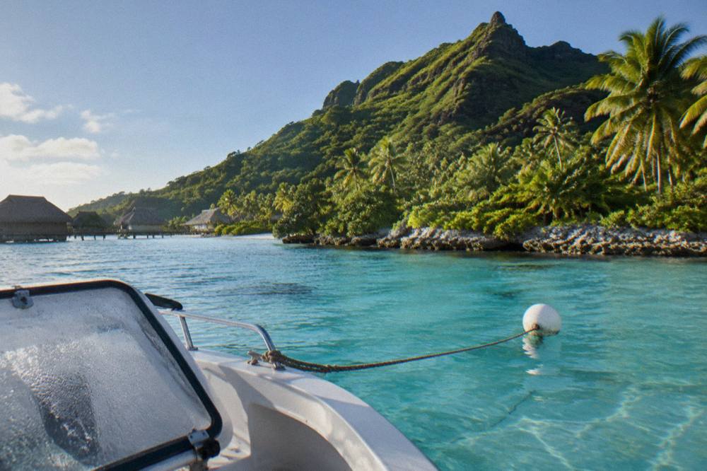A small boat moored over pale turquoise lagoon water beside a coral islet