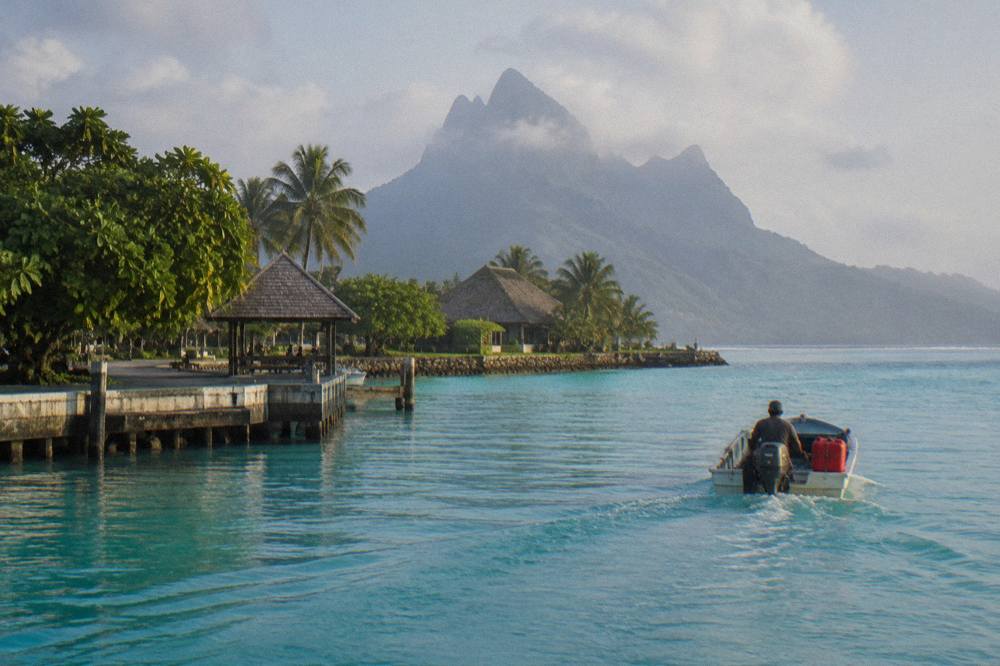 A small motorboat crossing calm turquoise lagoon water toward a reef