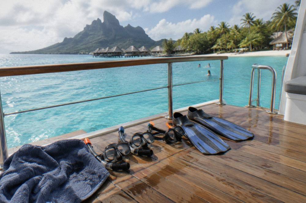 A guide's hands holding snorkel masks and fins on a wooden boat deck