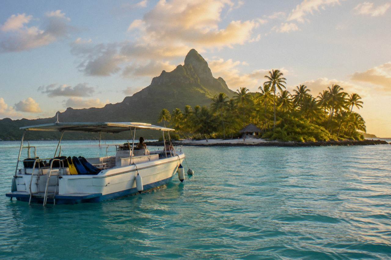 A snorkel boat moored over pale turquoise lagoon water near a green island peak