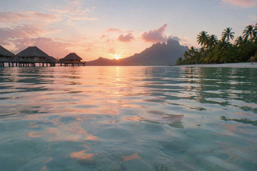 Flat calm lagoon at sunrise with soft light over turquoise water and a distant motu