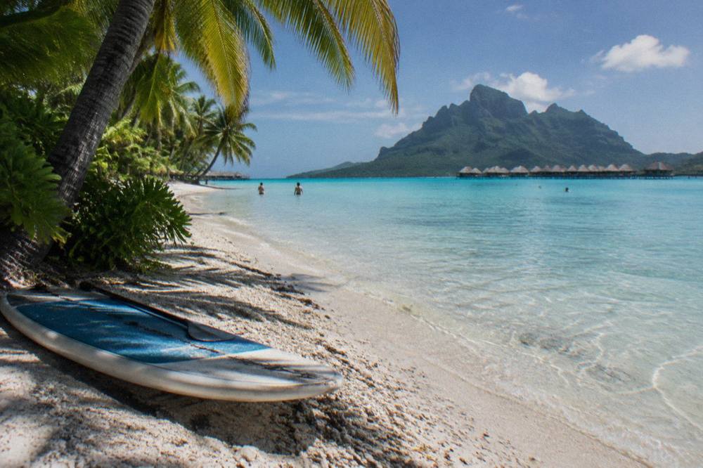 Shallow clear water over pale sand at a tropical beach with palm trees along the shore