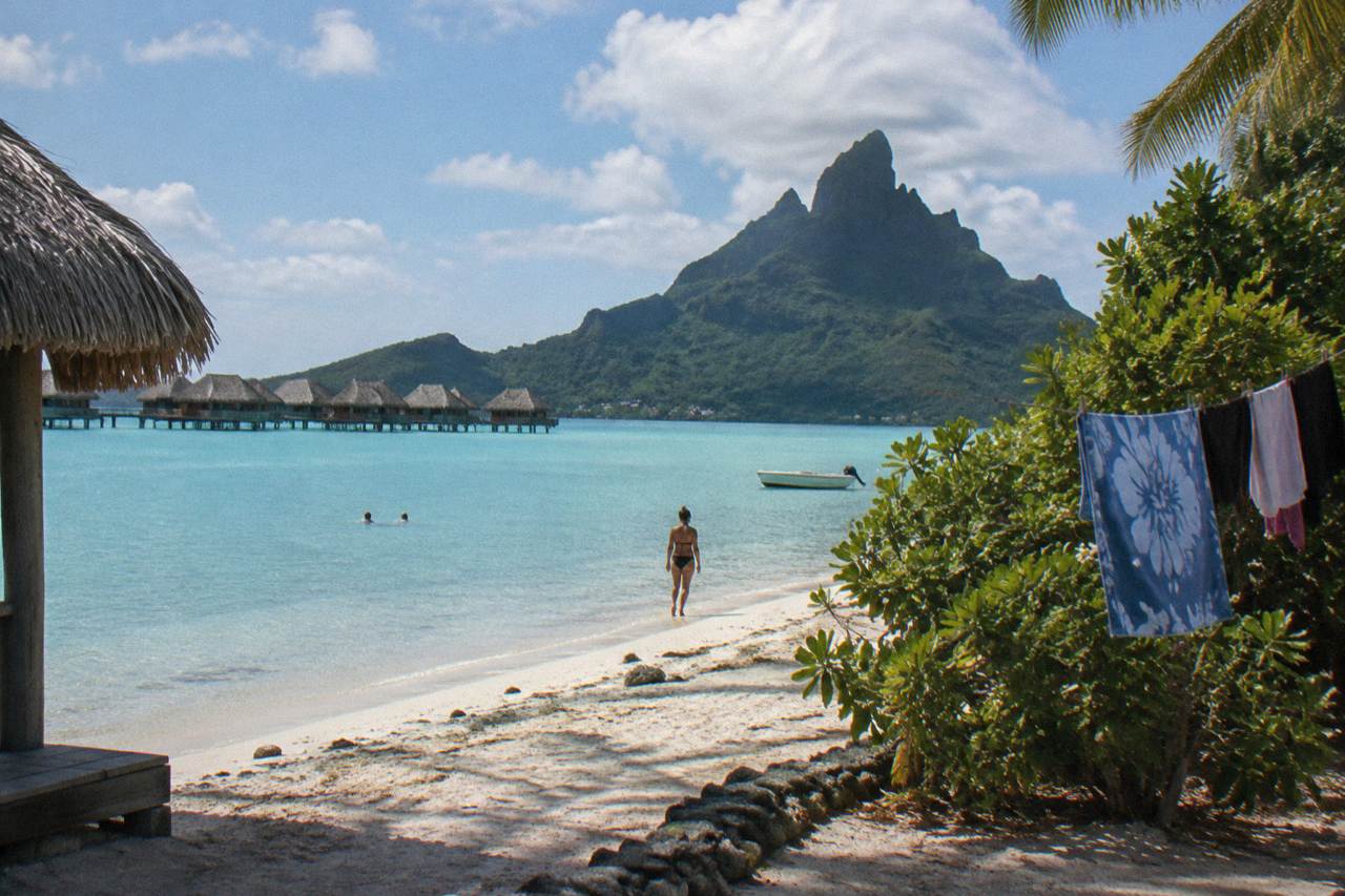 Calm turquoise lagoon water over pale sand at a tropical beach with a green volcanic peak behind