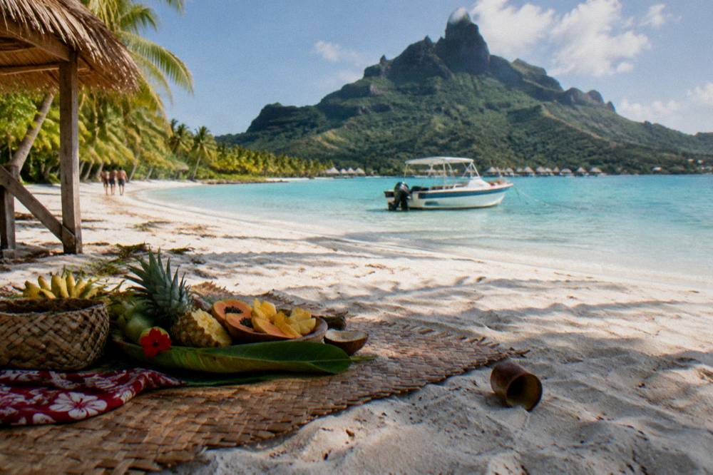 Boat anchored beside a palm-covered motu with lunch set up on the sand
