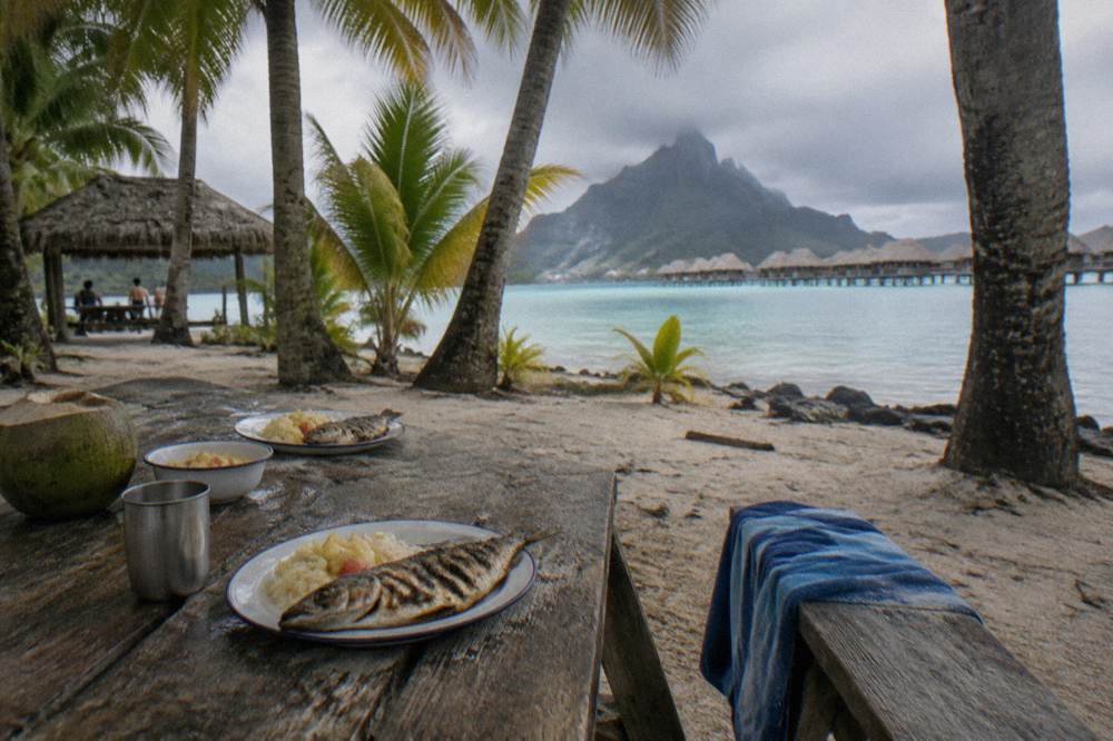 Wooden picnic table set with grilled lunch on a small sandy islet
