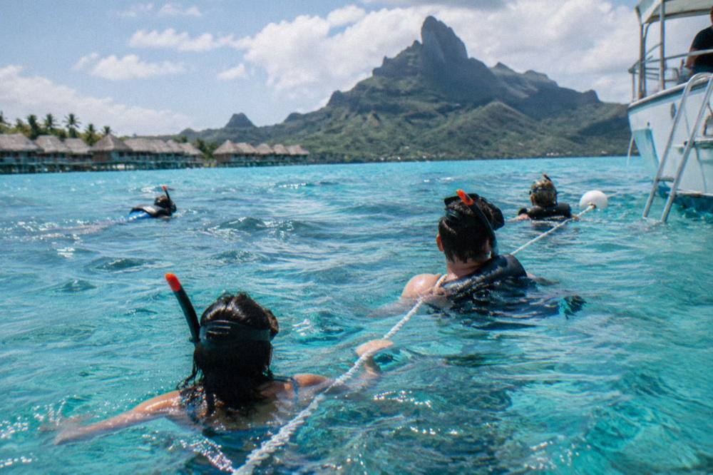 Group of snorkelers holding onto a floating line beside a boat in clear lagoon water