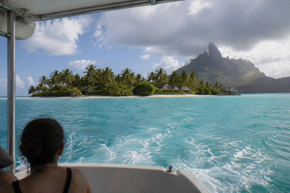 A covered lagoon tour boat crossing open turquoise water toward a reef islet