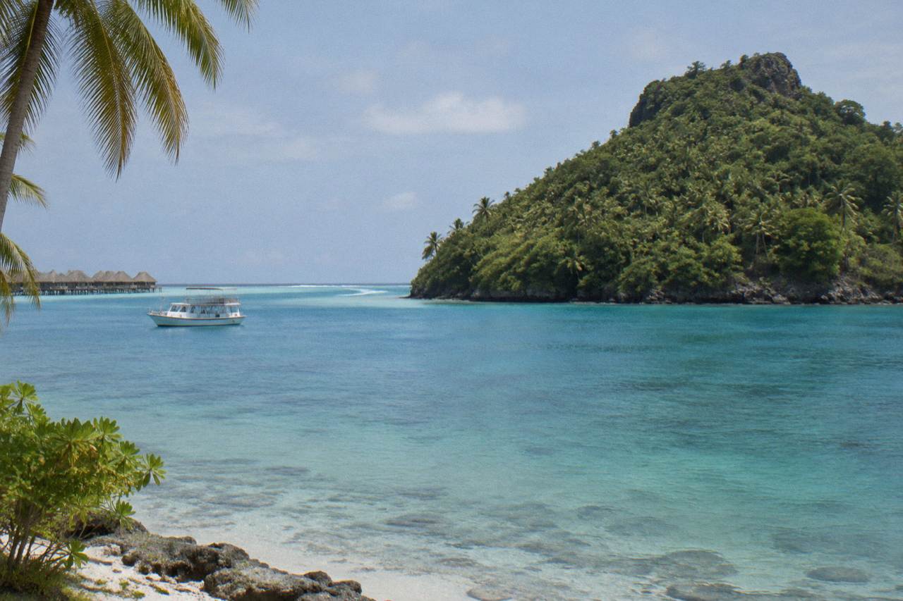 Turquoise lagoon water beside a green mountain island with a small boat anchored offshore