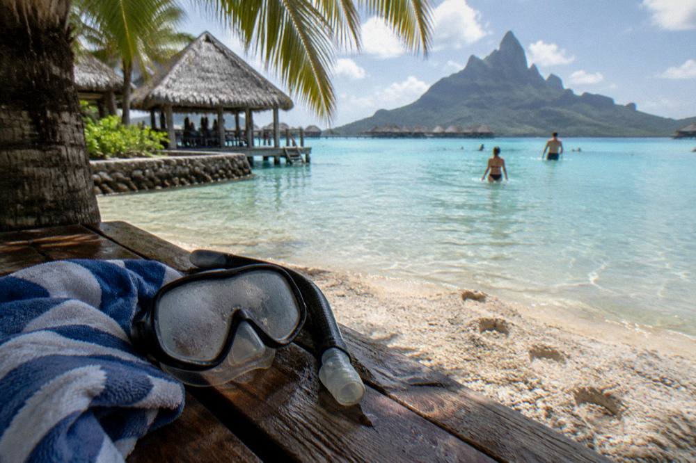 Snorkel mask and towel resting on a wooden bench under palm shade