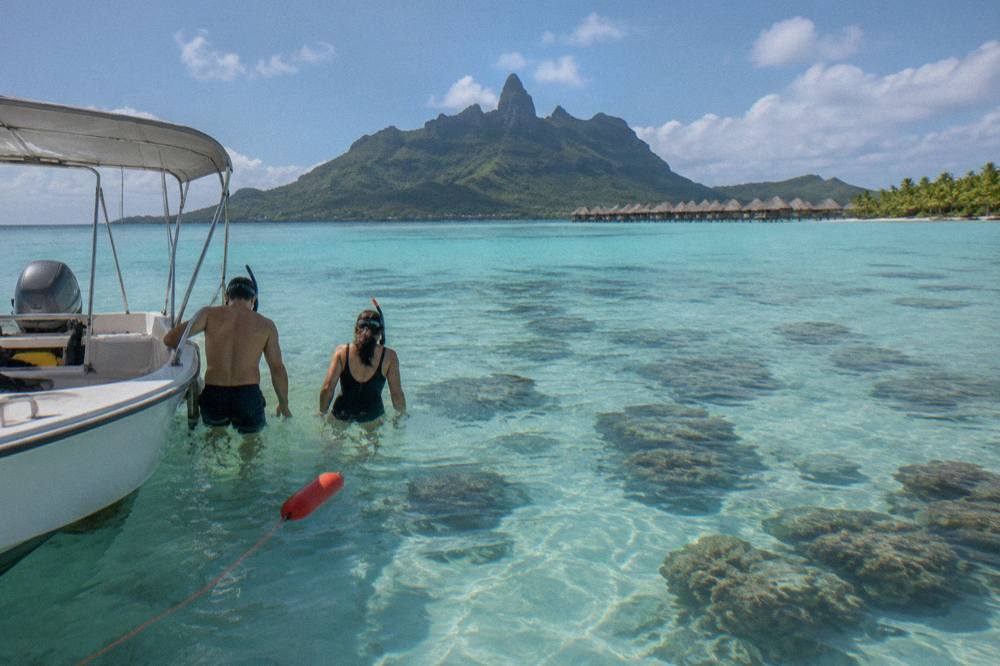 A small boat with snorkelers stopped over a shallow coral garden in turquoise lagoon water