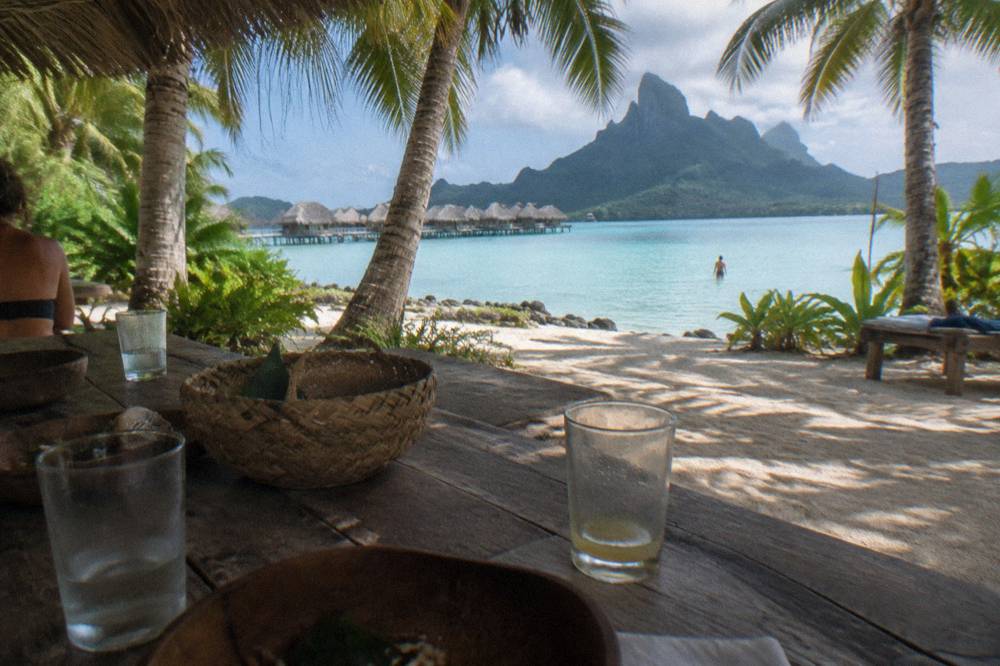 A shaded lunch table set on a sandy motu beside calm lagoon water