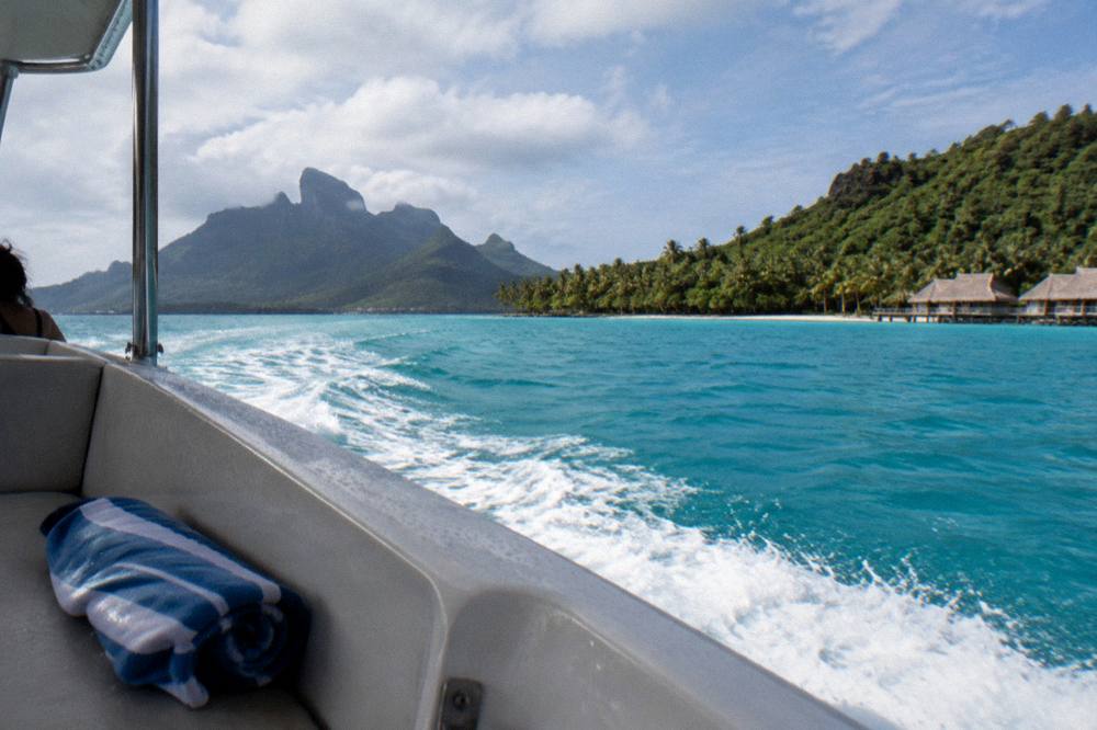 Boat crossing open lagoon water toward green volcanic peaks