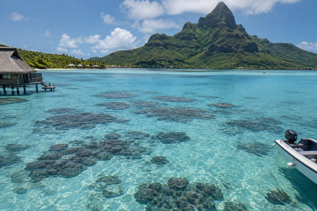 Turquoise lagoon water over coral formations with a green mountain peak in the background
