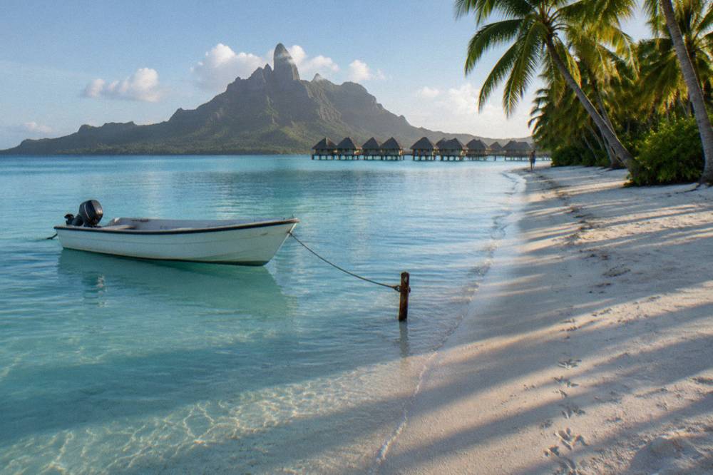 A small boat moored beside a sandy motu with palm trees in Bora Bora lagoon