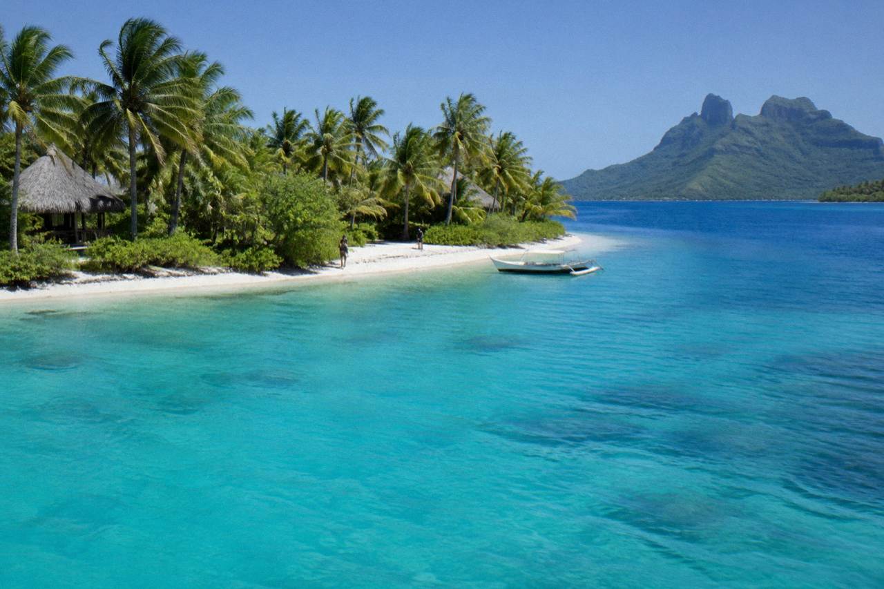 Turquoise lagoon water and green palm covered motu under a bright sky in Bora Bora