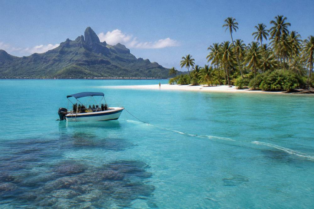 A small snorkel boat anchored beside a coral reef inside a turquoise lagoon