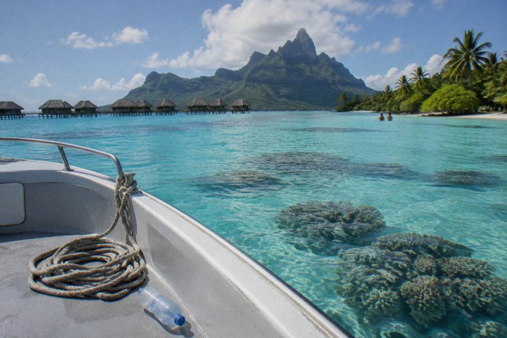 A small boat anchored over bright turquoise lagoon water near a coral garden