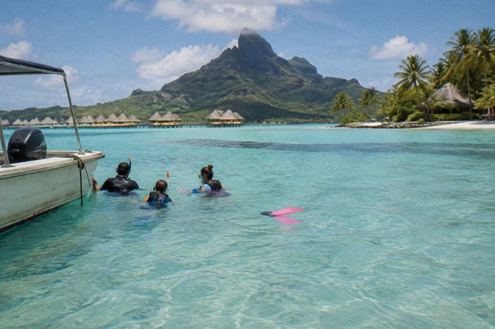 A family in snorkel gear floating beside a small boat in shallow lagoon water