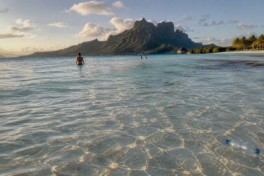 Shallow sandy lagoon shallows with rippled water and distant green motu