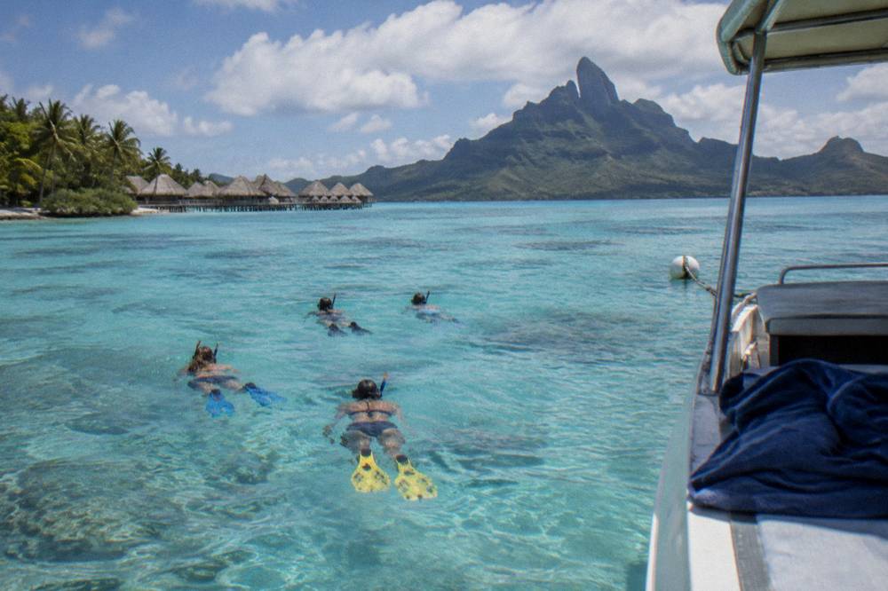 Snorkelers floating in bright shallow water beside a moored tour boat