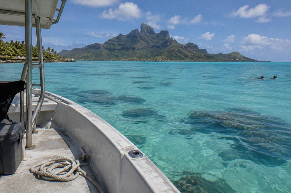 A small boat anchored over pale turquoise lagoon water beside a coral reef
