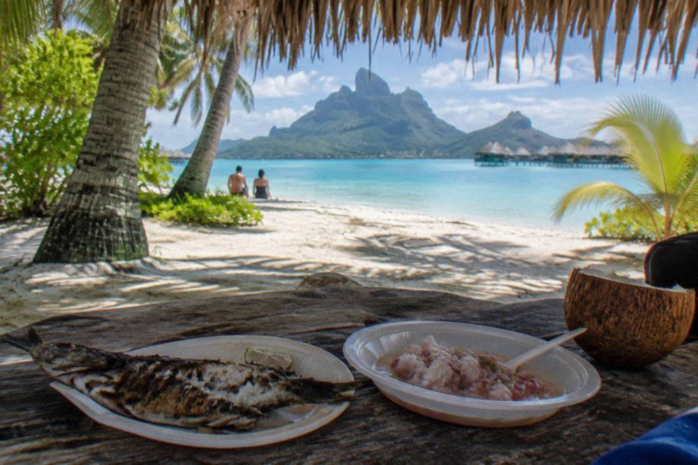 A shaded picnic table with a grilled lunch set out on a small sandy islet