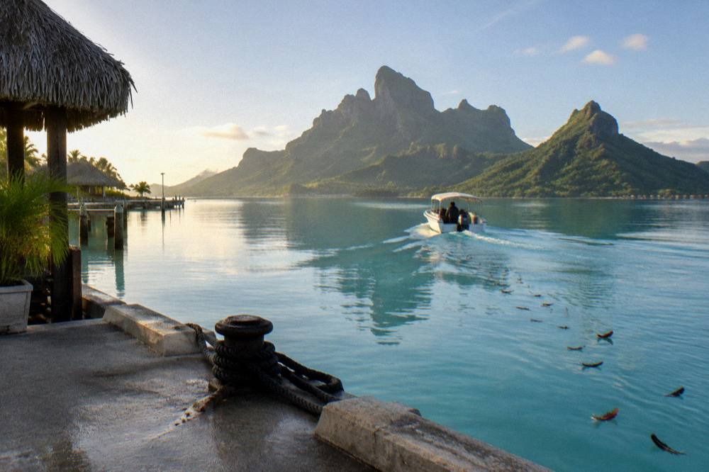 A boat crossing flat morning lagoon water toward green volcanic peaks