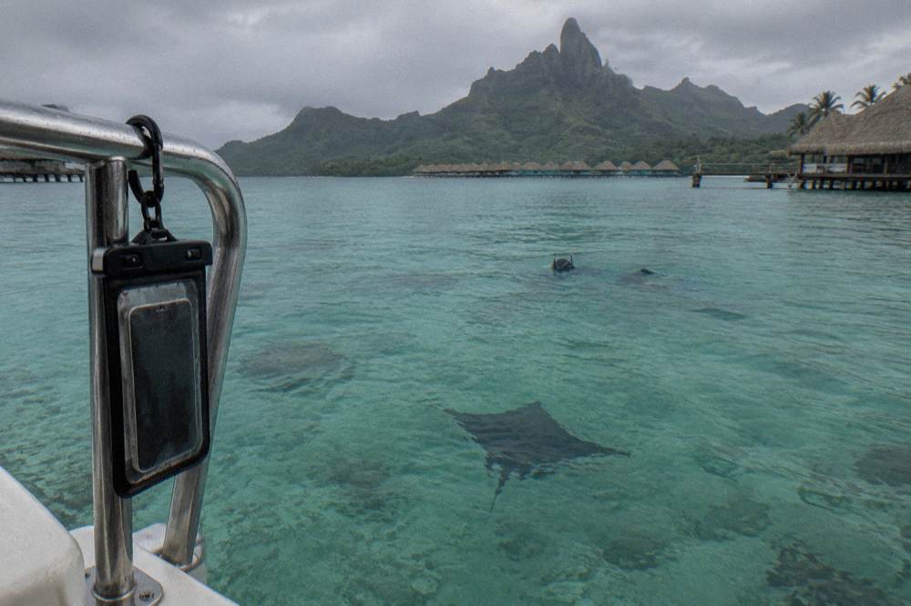 A waterproof phone pouch clipped to a boat rail above clear shallow lagoon water