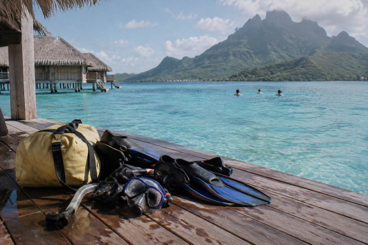 Snorkel gear and a dry bag resting on a boat deck beside turquoise lagoon water